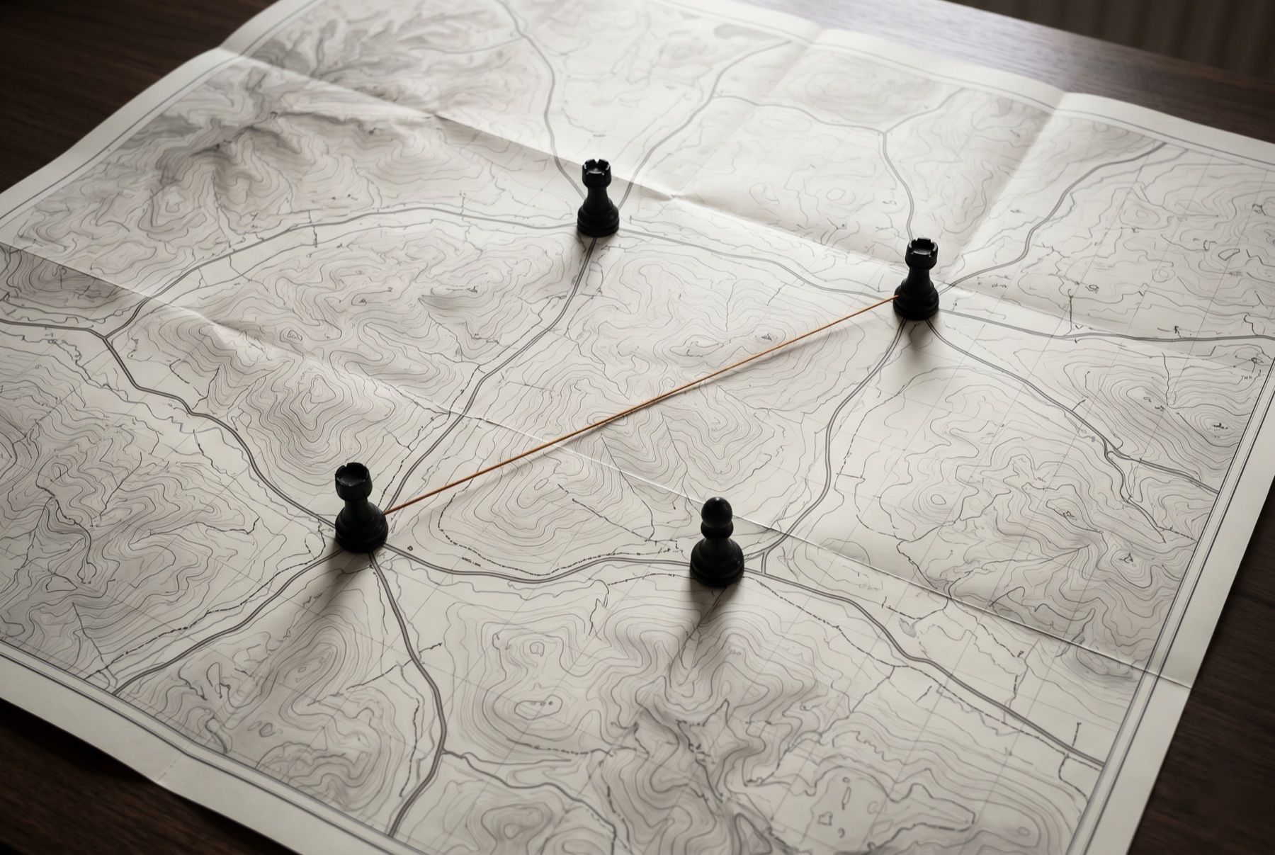 Topographic map with matte-black chess pieces connected by an amber thread — threat modelling and incident response