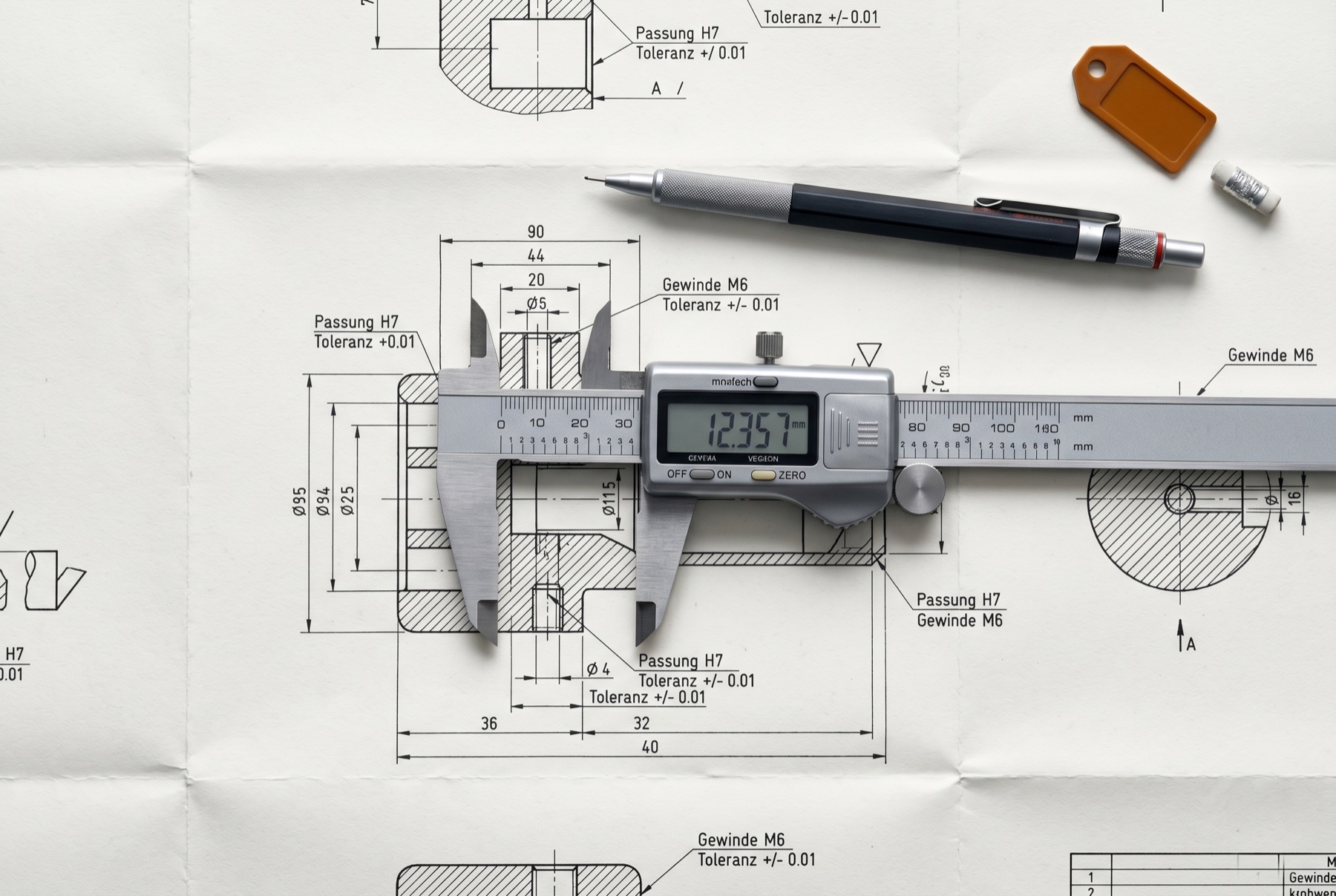 Digital caliper measuring a precision German engineering schematic with millimetre tolerances — software engineering rigor